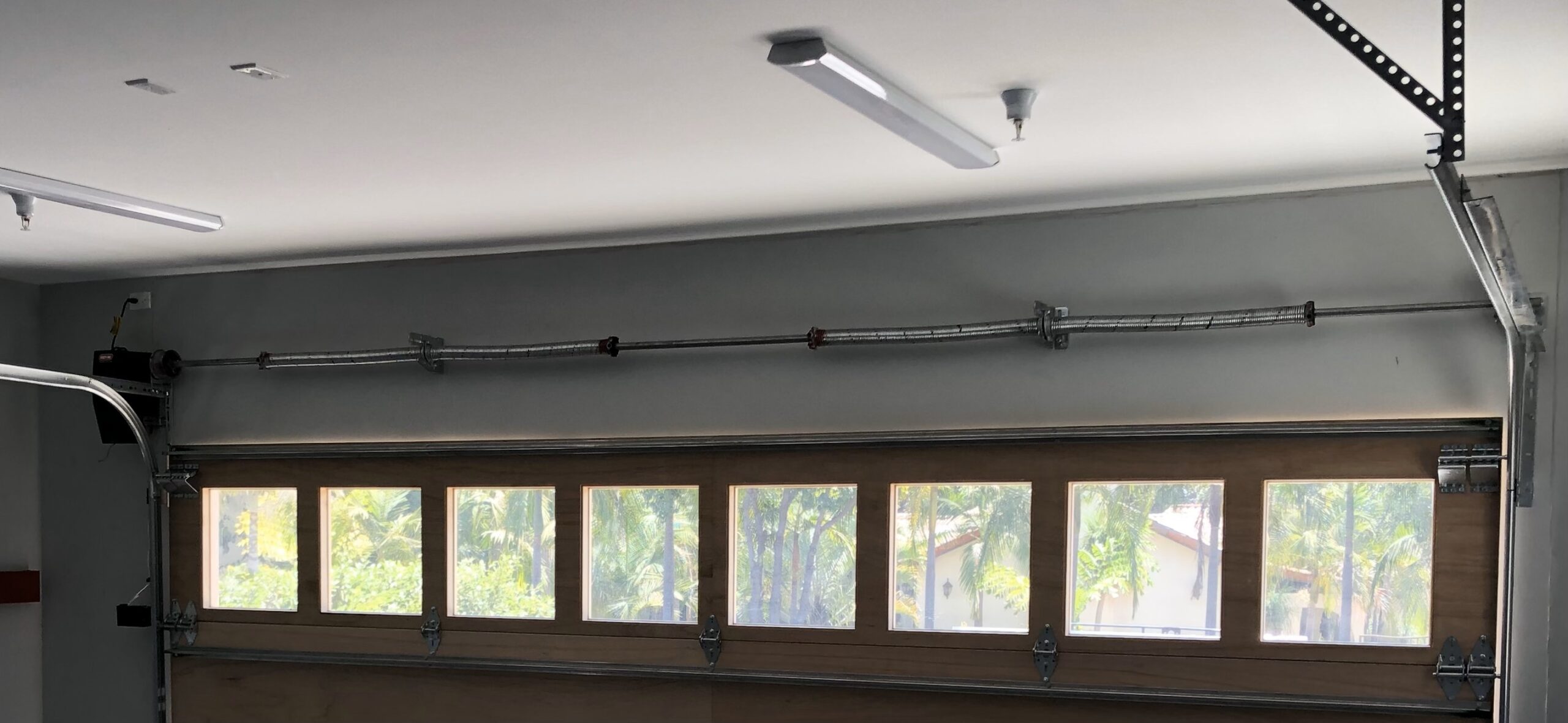 Quad spring system Interior view of a garage showing a wooden garage door with windows, ceiling-mounted track, and lighting above — modern garage door system setup.